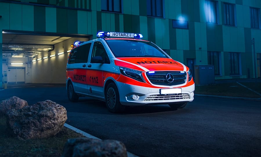 Notarzt-Einsatzfahrzeug des Rettungsdienstes mit aktivem Blaulicht vor einer Klinik in der Abenddämmerung.
