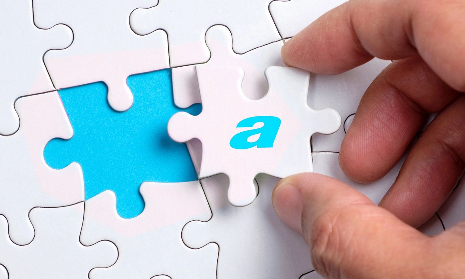Nahaufnahme einer Hand, die das letzte Puzzleteil in ein weißes Puzzle einfügt. Auf dem einzufügenden Teil ist der türkise Kleinbuchstabe 'a' (vom actiware-Logo) abgebildet. Die Lücke im Puzzle, in die das Teil passt, ist ebenfalls leuchtend Türkis, was die perfekte Ergänzung oder Lösung symbolisiert.